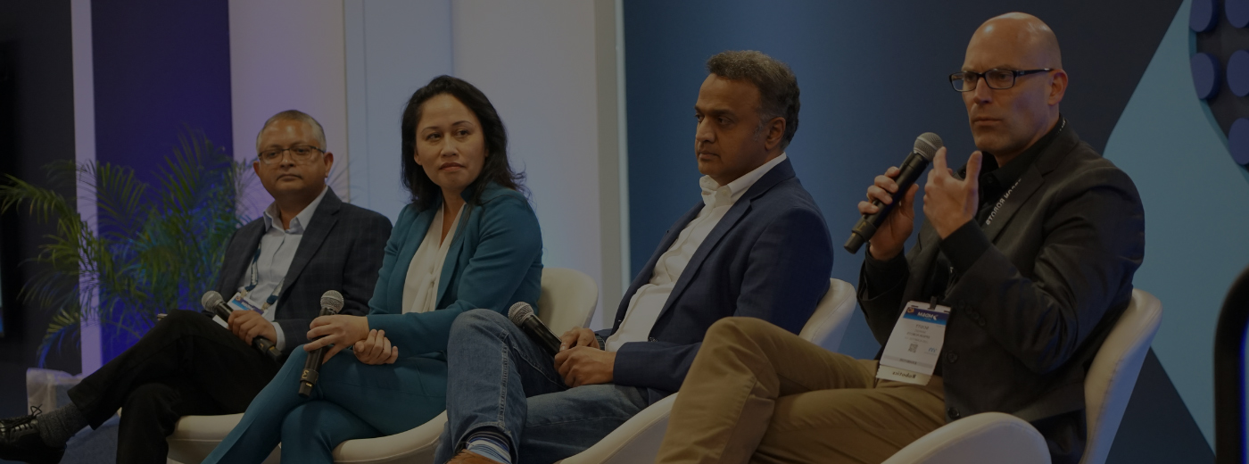  A group of four people sitting on chairs, positioned in front of a solid blue screen for a presentation