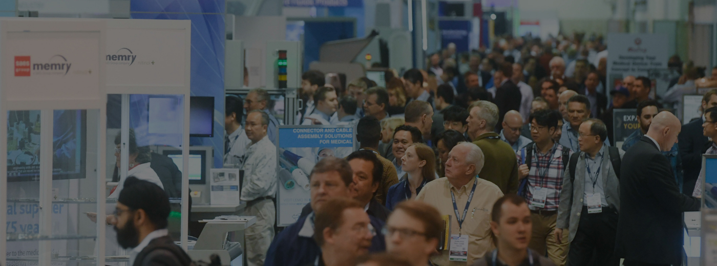 A diverse crowd of people walking through a bustling exhibition hall filled with displays and booths
