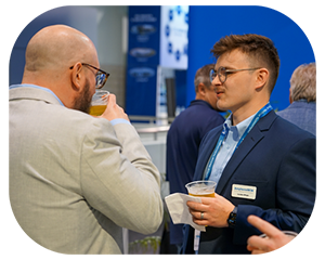 Two men engaged in conversation at a conference, surrounded by attendees and presentation materials