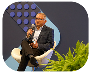 A man seated in a chair, speaking into a microphone during a presentation photo