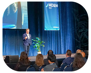 A man presenting at a conference, standing at a podium with a projector screen in the background displaying slides