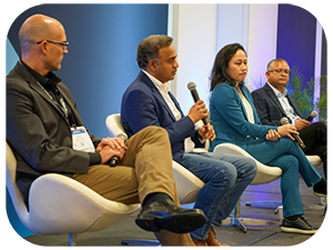 Four individuals seated on chairs, positioned in front of a microphone, engaged in a discussion or presentation