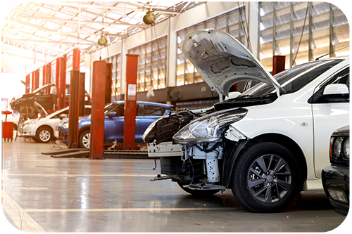 A car is elevated on a lift in a garage, with a mechanic inspecting the engine and various tools nearby