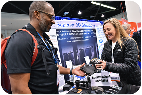 A man and woman at a trade show, both smiling while holding a product