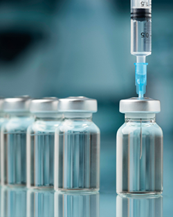 An image of a syringe drawing liquid from vaccine vials