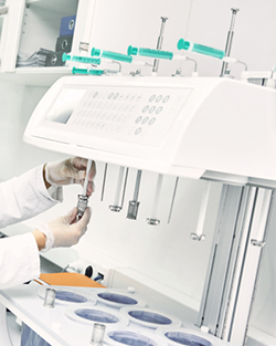 A woman in a lab coat is focused on her work in a laboratory, with various tools and equipment visible around her