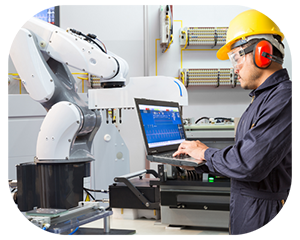 A man in a hard hat and safety glasses is engaged in work on a laptop, surrounded by construction materials