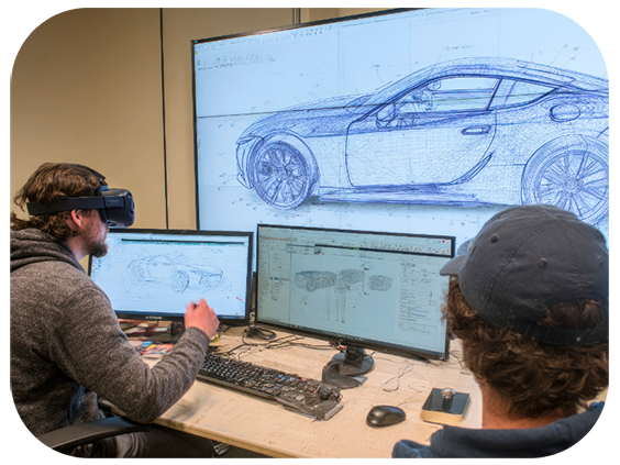 Two men wearing VR headsets are focused on a computer screen, engaged in a virtual experience together